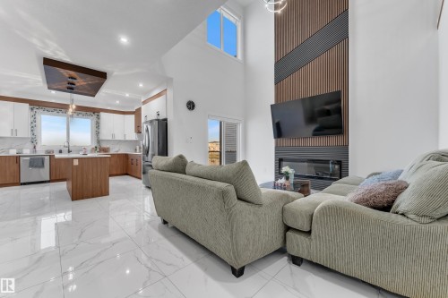 Vaulted ceiling with high windows, modern fireplace with a slatted accent wall, two-tone kitchen cabinetry, kitchen island, and stainless steel appliances - 6502 42 Ave, Beaumont, AB 