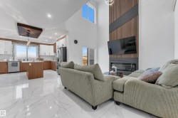 Vaulted ceiling with high windows, modern fireplace with a slatted accent wall, two-tone kitchen cabinetry, kitchen island, and stainless steel appliances - 