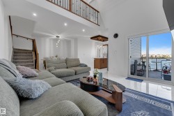 Two-story living area with high ceilings, recessed lighting, a built-in staircase with a wood railing and wrought iron balusters, and expansive sliding glass doors leading to an outdoor deck - 
