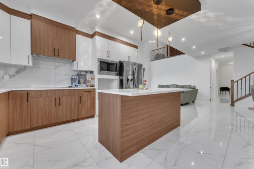 Kitchen featuring wood-finish cabinetry, white upper cabinets, stainless steel appliances, and a central island with a white countertop - 6502 42 Ave, Beaumont, AB 