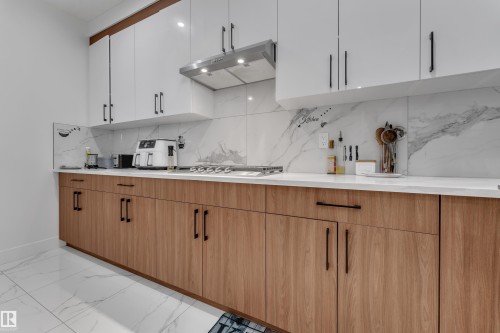 Modern kitchen with two-tone cabinetry, a built-in cooktop, and a stainless steel range hood - 6502 42 Ave, Beaumont, AB 