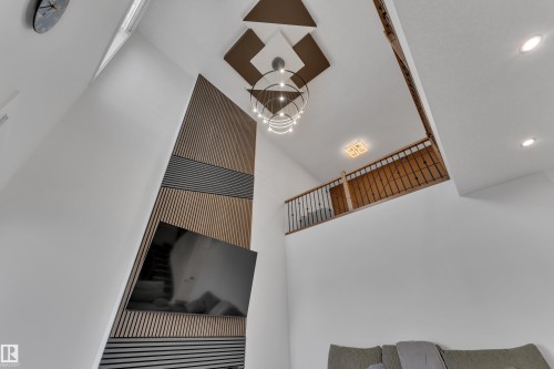 Vaulted ceiling with a contemporary chandelier, two-story accent wall with wood-finish paneling, recessed lighting, and a second-story interior balcony with an iron railing - 6502 42 Ave, Beaumont, AB 