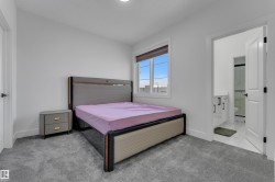 Carpeted bedroom with a window, white walls, and an attached three-piece bathroom with a single vanity and glass-enclosed shower - 
