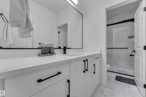 White vanity with black hardware, white countertop, large wall-mounted mirror, and a shower with glass enclosure and tiled walls - 6502 42 Ave, Beaumont, AB 