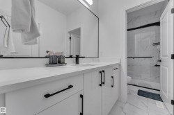 White vanity with black hardware, white countertop, large wall-mounted mirror, and a shower with glass enclosure and tiled walls - 