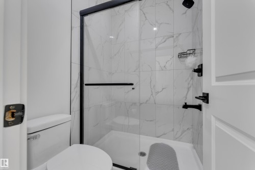 Tiled shower enclosure with a glass door, matte black fixtures, and a white toilet - 6502 42 Ave, Beaumont, AB 