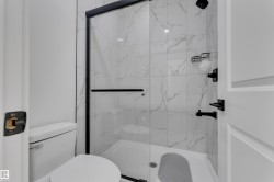 Tiled shower enclosure with a glass door, matte black fixtures, and a white toilet - 