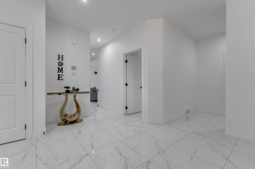 White tile flooring with veining, white walls, recessed lighting, and white interior doors with dark hardware - 6502 42 Ave, Beaumont, AB 