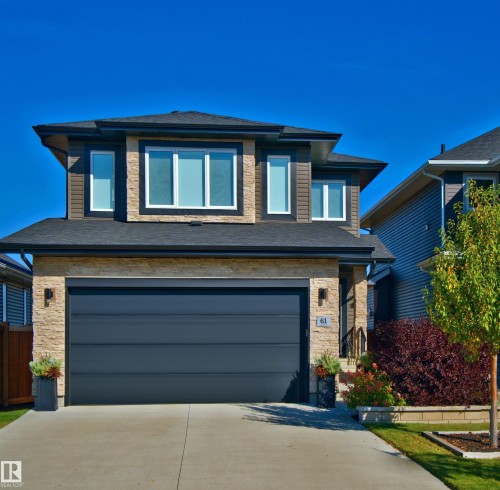 Modern two-story exterior featuring stone and horizontal siding, an attached garage, a paved driveway, and established landscaping - 61 Encore Crescent, St. Albert, AB 