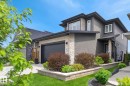 Contemporary multi-story exterior with stone and siding accents, featuring an integrated garage and a landscaped front yard with retaining walls - 61 Encore Crescent, St. Albert, AB 