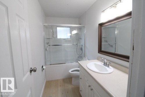 Bathroom featuring a single vanity with an integrated sink, wood-finish flooring, and a tub with a sliding glass enclosure - 44 Arlington Drive, St. Albert, AB 