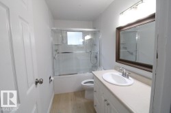 Bathroom featuring a single vanity with an integrated sink, wood-finish flooring, and a tub with a sliding glass enclosure - 