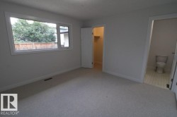 Wall-to-wall carpeting, large window with white trim, private backyard fencing, adjacent built-in closet with shelving, and an en-suite bathroom with tiled flooring - 