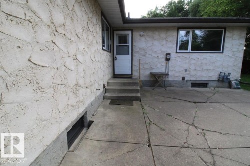 Exterior featuring textured stucco siding, white-framed windows, a white entry door, and a concrete patio - 44 Arlington Drive, St. Albert, AB 