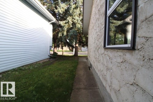 Stucco exterior, black-framed window, concrete pathway, and mature trees - 44 Arlington Drive, St. Albert, AB 