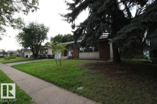 Brick and stone facade with large windows, mature trees, and a concrete pathway - 44 Arlington Drive, St. Albert, AB 