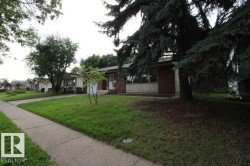 Brick and stone facade with large windows, mature trees, and a concrete pathway - 
