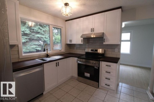 Updated kitchen featuring white shaker cabinetry, dark countertops, stainless steel appliances, a subway tile backsplash, and tile flooring - 44 Arlington Drive, St. Albert, AB 