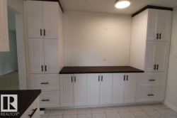 White shaker-style cabinetry with dark wood-finish countertops, tile flooring, and integrated overhead lighting - 