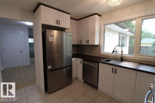 White shaker-style cabinetry with dark hardware, stainless steel appliances, dark wood-finish countertops, ceramic tile backsplash, and a double-basin stainless steel sink with a high-arc faucet - 44 Arlington Drive, St. Albert, AB 