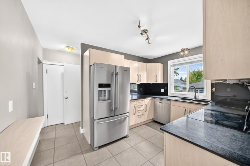 Kitchen featuring light wood-finish cabinetry, dark countertops, tile flooring, and stainless steel appliances - 10715 133 Street Nw, Edmonton, AB 