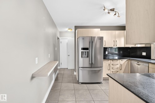 Stainless steel French door refrigerator, track lighting, light wood-finish cabinetry, dark countertops, and tile flooring - 10715 133 Street Nw, Edmonton, AB 