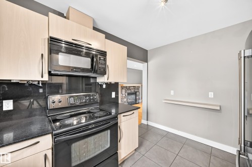 Kitchen featuring light wood-finish cabinetry, dark countertops, black appliances, and gray floor tiling - 10715 133 Street Nw, Edmonton, AB 
