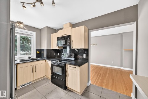 Kitchen featuring light wood-finish cabinetry, black countertops, and a black tile backsplash - 10715 133 Street Nw, Edmonton, AB 
