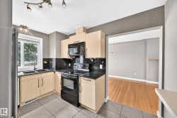 Kitchen featuring light wood-finish cabinetry, black countertops, and a black tile backsplash - 