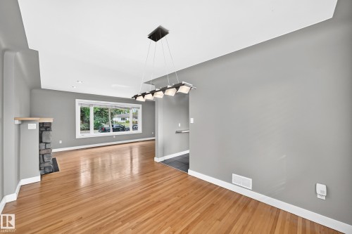 Hardwood flooring, stone fireplace with wood mantel, large picture window, recessed lighting, and contemporary linear chandelier - 10715 133 Street Nw, Edmonton, AB 