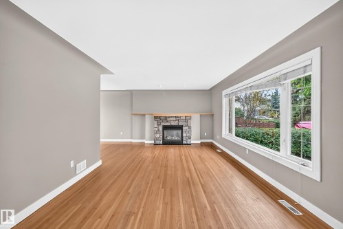 Hardwood flooring, stone-clad fireplace with wood mantel, large bay window, and neutral wall tones - 10715 133 Street Nw, Edmonton, AB 