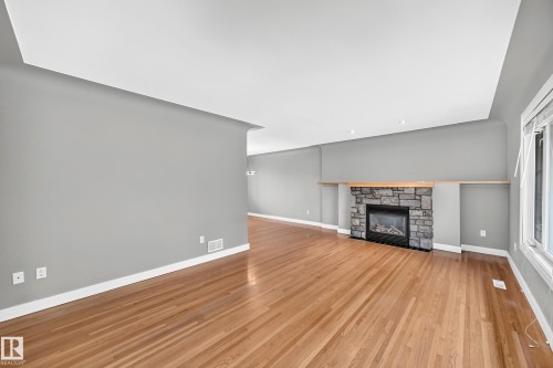 Spacious interior featuring wood-finish flooring, a stone-surround fireplace with a wood mantle, recessed lighting, and a tray ceiling - 10715 133 Street Nw, Edmonton, AB 