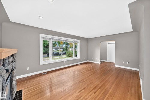 Hardwood flooring, recessed ceiling lighting, a stone fireplace with a wood mantel, an arched entryway, and a large picture window - 10715 133 Street Nw, Edmonton, AB 