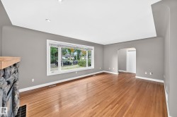 Hardwood flooring, recessed ceiling lighting, a stone fireplace with a wood mantel, an arched entryway, and a large picture window - 