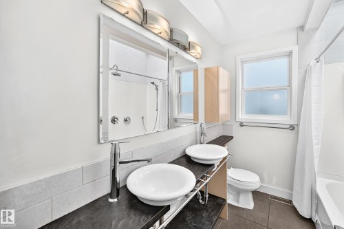 Double vessel sinks with chrome fixtures, large mirror, and tiled walls - 10715 133 Street Nw, Edmonton, AB 