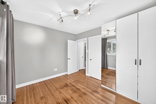 Wood-finish flooring with white baseboards, track lighting, light grey wall paint, and white built-in cabinetry with mirrored panels - 10715 133 Street Nw, Edmonton, AB 