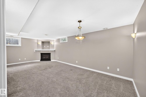 Recessed fireplace with mantel and sconce lighting, neutral wall color, recessed ceiling, and a hanging pendant light fixture - 10715 133 Street Nw, Edmonton, AB 