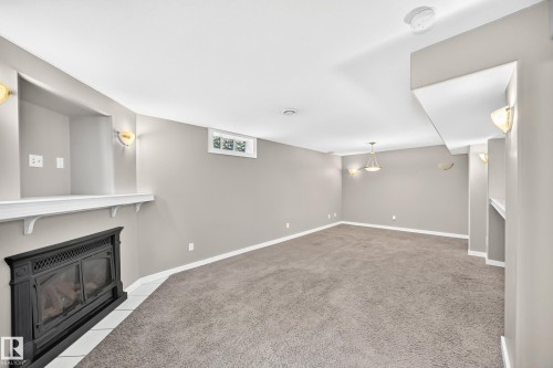 Spacious carpeted room featuring a fireplace with a white mantel, recessed display niche, and wall sconces - 10715 133 Street Nw, Edmonton, AB 