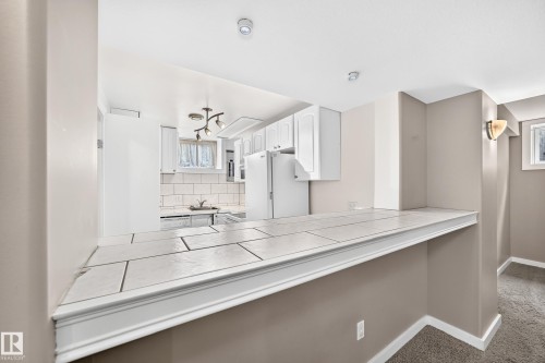 Kitchen with white cabinetry, tile backsplash, and a tiled breakfast bar - 10715 133 Street Nw, Edmonton, AB 