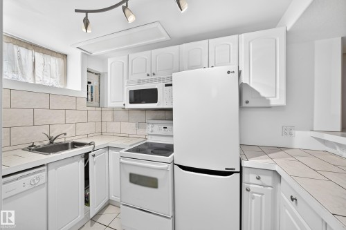 Kitchen featuring white cabinetry, tile countertops, stainless steel sink, over-range microwave, and built-in dishwasher - 10715 133 Street Nw, Edmonton, AB 