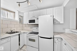 Kitchen featuring white cabinetry, tile countertops, stainless steel sink, over-range microwave, and built-in dishwasher - 