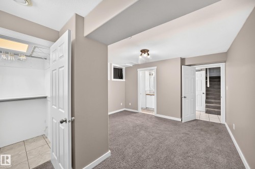 Carpeted room with a ceiling-mounted light fixture, white trim, and a white paneled door leading to a tiled closet with a shelf - 10715 133 Street Nw, Edmonton, AB 
