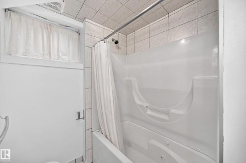 White tiled bathroom with a window, built-in tub, and tiled wall accents - 10715 133 Street Nw, Edmonton, AB 
