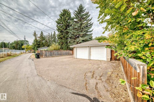 Detached two-car garage with two white garage doors, asphalt shingle roof, and wood fencing - 10715 133 Street Nw, Edmonton, AB 