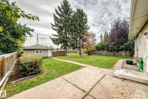 Expansive backyard featuring a detached garage, mature trees, concrete pathways, and a partial wooden fence - 10715 133 Street Nw, Edmonton, AB 