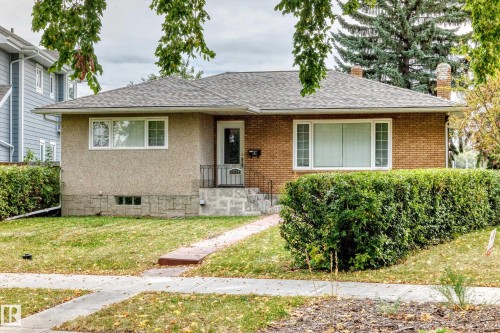 Brick and stucco exterior with a composite shingle roof, featuring a concrete walkway and mature shrubbery - 10715 133 Street Nw, Edmonton, AB 