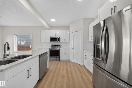 Modern kitchen featuring stainless steel appliances, white cabinetry, wood-finish flooring, and a double basin sink - 7836 7 Ave Sw Sw, Edmonton, AB 