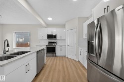 Modern kitchen featuring stainless steel appliances, white cabinetry, wood-finish flooring, and a double basin sink - 