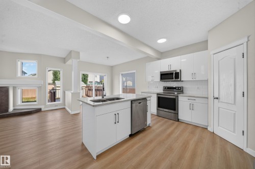 Kitchen featuring a center island with double sink, stainless steel appliances, white cabinetry, and light wood-finish flooring - 7836 7 Ave Sw Sw, Edmonton, AB 