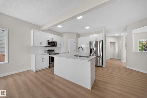 Modern kitchen featuring white cabinetry, stainless steel appliances, a center island with sink, quartz countertops, and wood-finish flooring - 7836 7 Ave Sw Sw, Edmonton, AB 